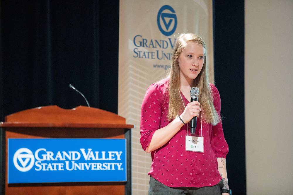 Student speaking to the audience, standing to the side of a GVSU podium